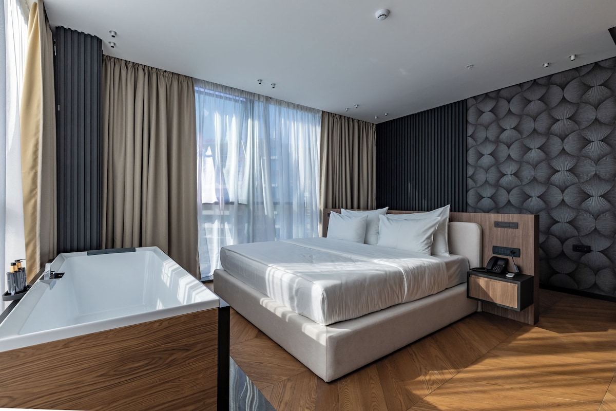 A modern hotel room with a large bed, a wooden floor, a nightstand, and a wall-mounted phone.
