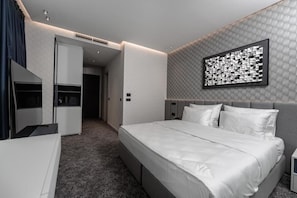 Moderni hotellihuone, jossa on suuri sänky, vaatekaappi, työpöytä ja seinälle asennettu taideteos.