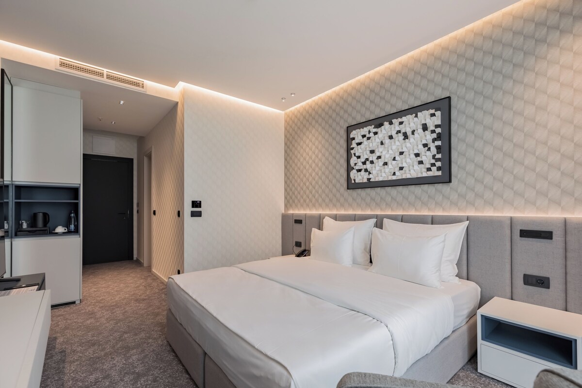 Una habitación de hotel moderna con una cama grande, mesitas de noche, un armario y una obra de arte colgada en la pared.