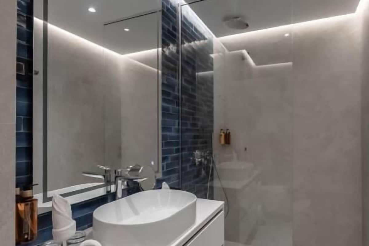 A modern bathroom with a large mirror, a white sink, and a glass shower enclosure.