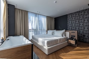 Moderni hotellihuone, jossa on suuri sänky, puulattia, yöpöytä ja seinälle asennettu puhelin.