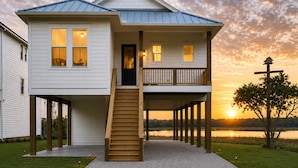 Una casa de dos pisos con un balcón, una escalera que lleva a la entrada y vista al lago al atardecer.