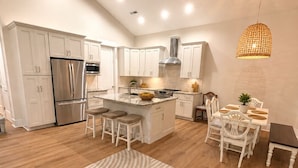 Una cocina moderna con armarios blancos, un refrigerador de acero inoxidable y una isla central con taburetes.