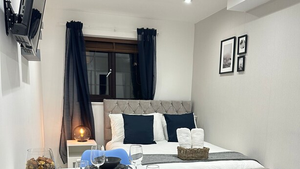 A compact hotel room with a bed, a desk with chairs, a TV mounted on the wall, and a small table set for dining. - The Tower Bridge Hidden Gem (London)
