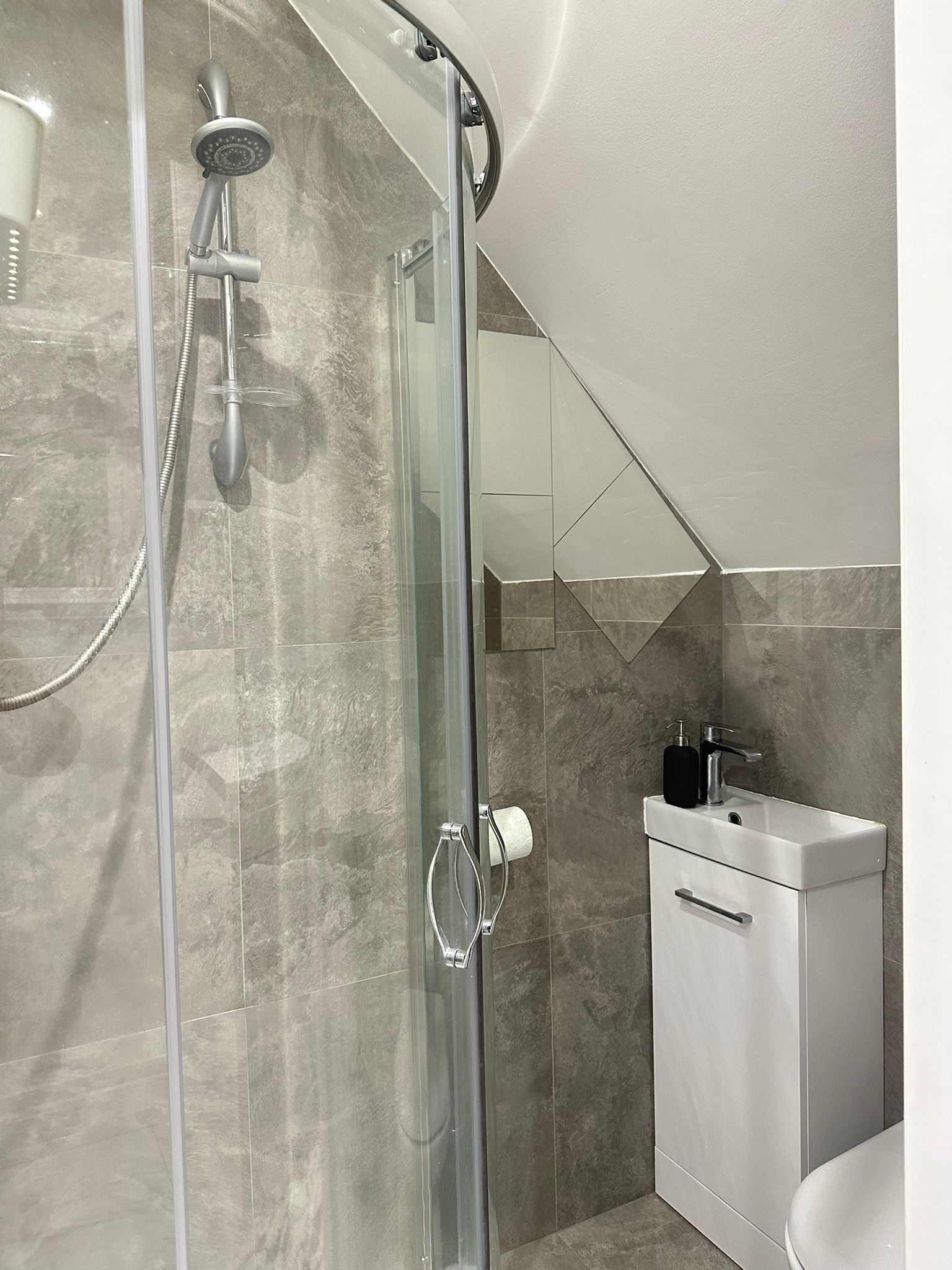 A modern bathroom with a glass shower enclosure, a white sink, and a mirror.
