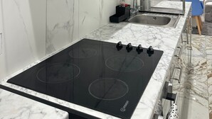 A modern kitchen with a black induction cooktop, a stainless steel range hood, and a marble backsplash. - The Tower Bridge Hidden Gem (London)
