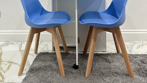 A dining area with a table, two blue chairs, a TV mounted on the wall, and a decorative light fixture. - The Tower Bridge Hidden Gem (London)