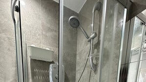 A glass-enclosed shower stall with a handheld showerhead, a wall-mounted faucet, and a toilet paper holder on the right. - The Tower Bridge Hidden Gem (London)