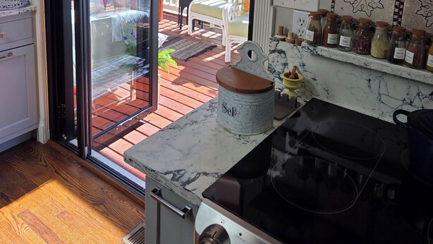 A kitchen with a stove, a glass door leading to a patio, and shelves with jars. - Superb_Suburban_Summer (Herndon)