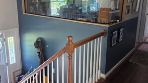 A staircase with white balusters and a wooden handrail, leading to a room with a large mirror and a view of the outdoors. - Superb_Suburban_Summer (Herndon)