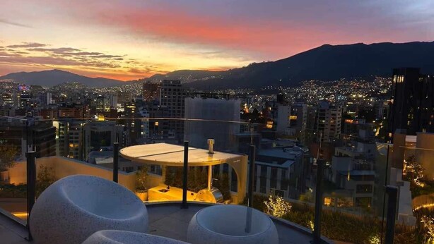 A rooftop terrace with a seating area, a glass enclosure, and a view of a cityscape at dusk. - Vista hermosa la carolina 14th floor (Quito)