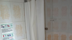 A bathroom with a toilet, shower curtain, and tiled walls. - HOTEL DEL PUENTE BOGOTA (Bogotá)