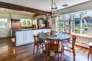 A kitchen with a large island, wooden chairs, and a view through large windows. - Adorable Ram Island Water View Home & Guest Cottage with beach access (Shelter Island)