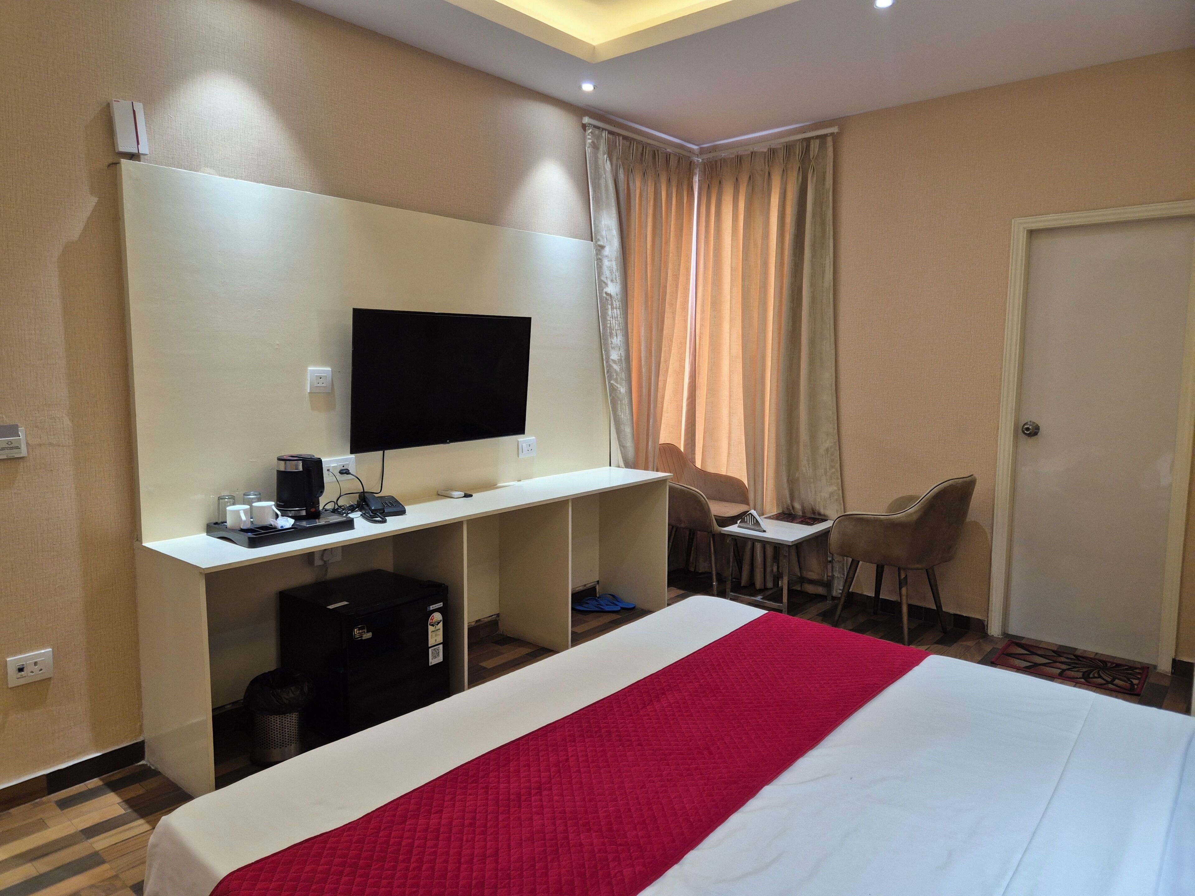 A hotel room with a bed, a desk with a computer, a TV, and two chairs.