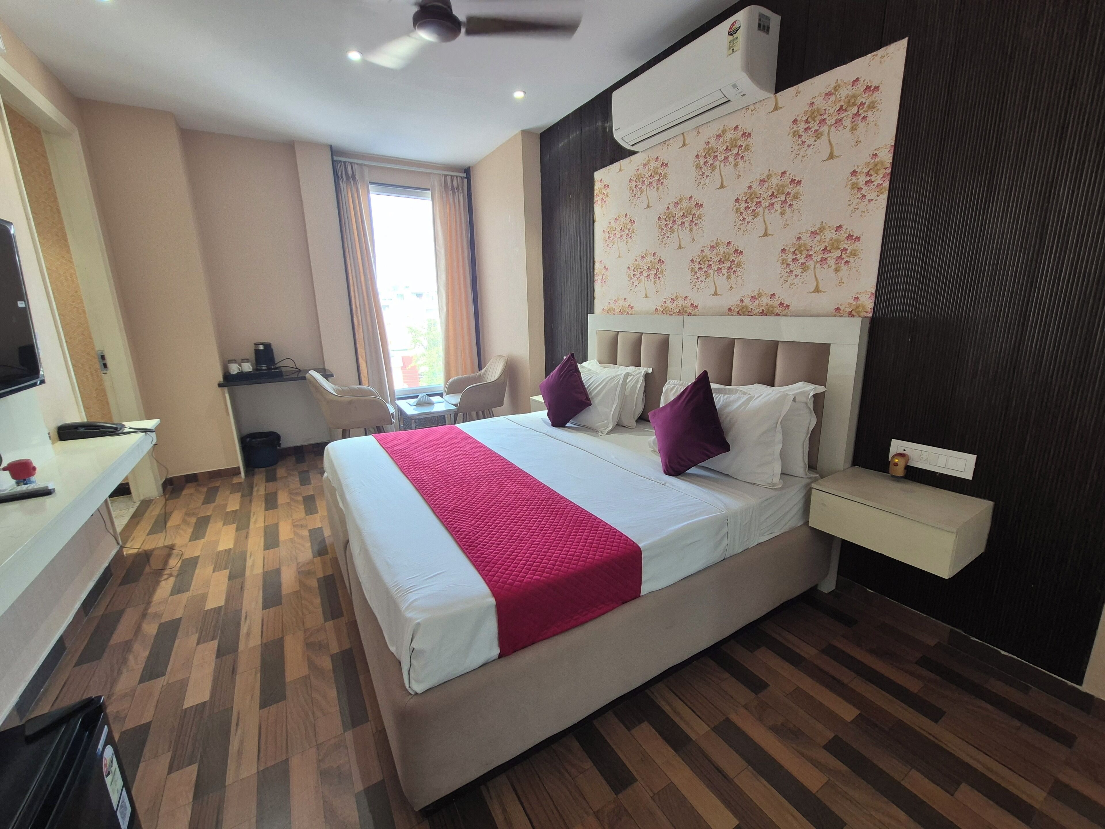 Habitación de hotel con cama, escritorio, silla, equipo de aire acondicionado y ventana con cortinas.