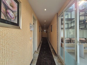 Un pasillo con paredes decoradas, cuadros enmarcados y una puerta de cristal que da a una habitación con estanterías.