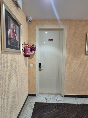 A hotel entrance with a door marked '305', a security camera, a framed advertisement, and a fire extinguisher. - OnlyStay Ginger Palace Sector 19 Noida (Noida)