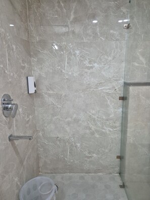 Un baño con suelo de mármol, cabina de ducha de vidrio, inodoro y secamanos.