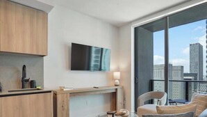 Una cocina moderna con televisor de pantalla plana, un comedor con mesa y sillas, y un balcón con vista a la ciudad.