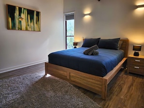 Une chambre à coucher avec un lit, une table de chevet, une lampe, un tableau et une fenêtre.