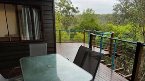 Une terrasse avec une table et des chaises, une fenêtre avec des rideaux et une vue sur une zone boisée.