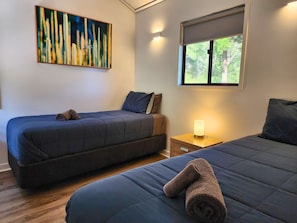 A bedroom with two beds, a nightstand, a wall-mounted lamp, and a painting.