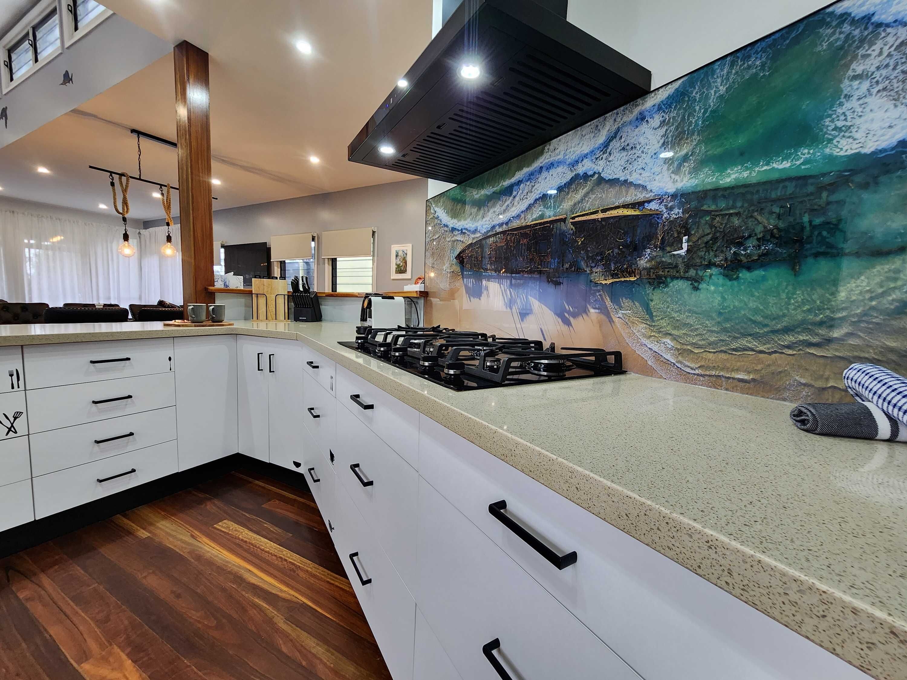 A modern kitchen with white cabinets, a gas stove, and a large mural of a beach scene.