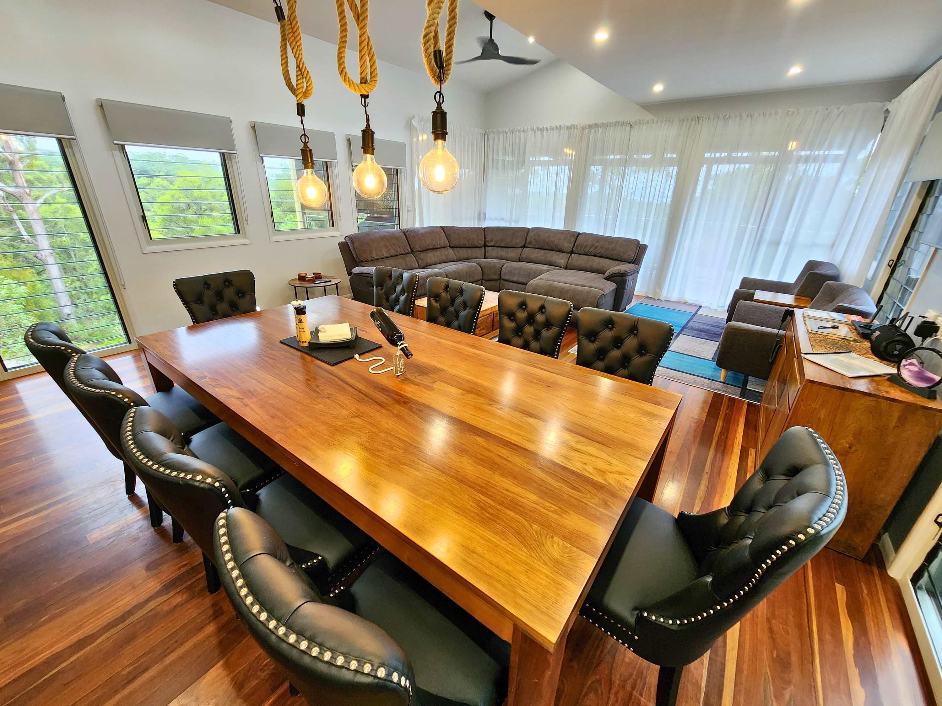 A dining area with a wooden table, black upholstered chairs, a brown sofa, and a ceiling fan.
