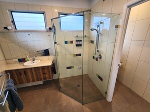 Ett modernt badrum med en dusch med glasväggar, ett handfat med spegel och en kommod i trä.