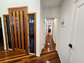 A hallway with wooden flooring, white walls, and a door with a glass panel. - Bushy s Hilltop Kingfisher Bay K Gari Fraser Island (K'gari (Fraser Island))
