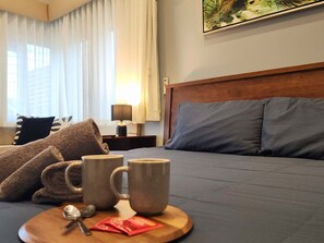 A hotel room with a bed, a bedside table with a lamp, a tray with mugs and a spoon, and a window with curtains. - Bushy s Hilltop Kingfisher Bay K Gari Fraser Island (K'gari (Fraser Island))