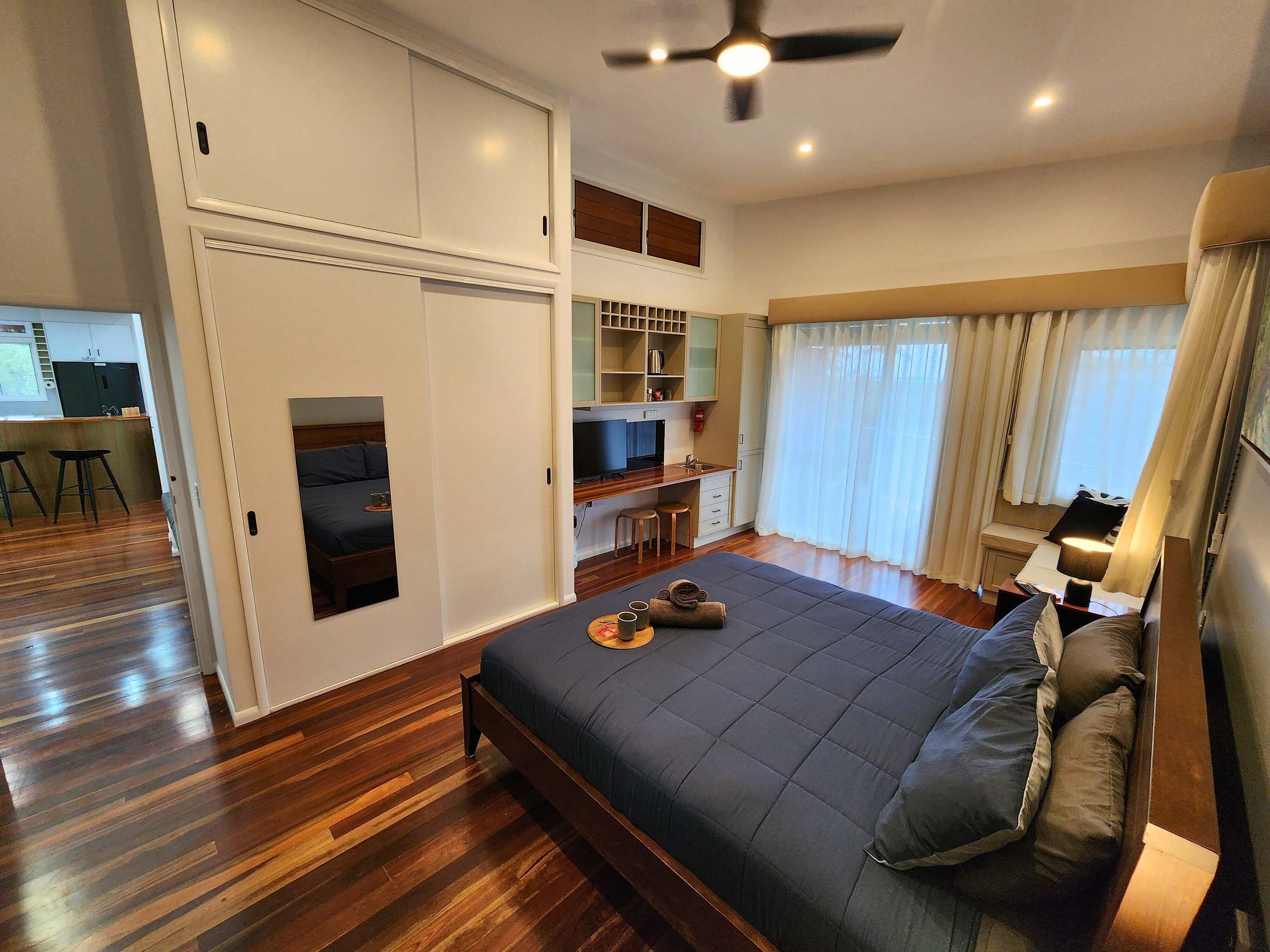 A bedroom with a bed, a desk, a chair, a television, and a window with curtains.