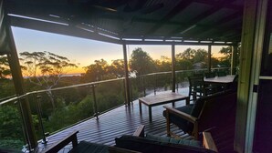 Un espace extérieur aménagé, abrité et doté de sièges, offrant une vue sur les arbres et le coucher du soleil.
