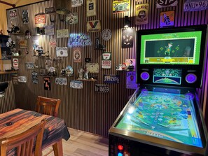 Máquina de pinball com tema retrô, cercada por placas de carro antigas e letreiros de neon numa parede de madeira.