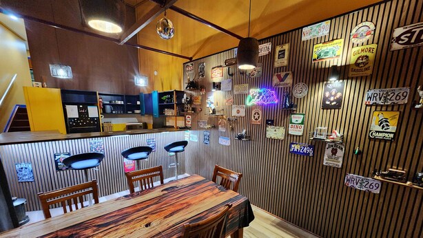 Un restaurant au décor intérieur en bois, avec un bar et un mur orné de plaques d’immatriculation anciennes et d’enseignes au néon.