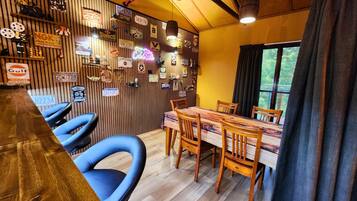 A dining area with a wooden table and chairs, a wooden wall with various signs, and a window with curtains.