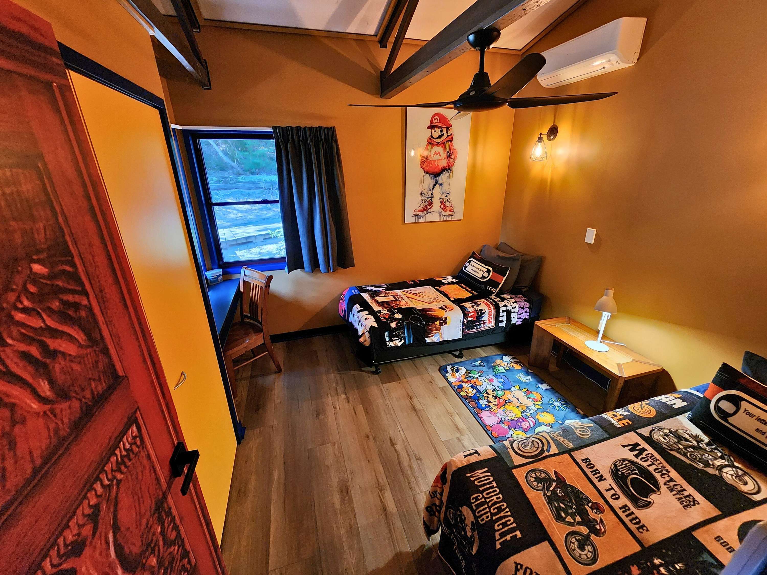 A bedroom with a bed, a desk, a chair, a window, and a ceiling fan.