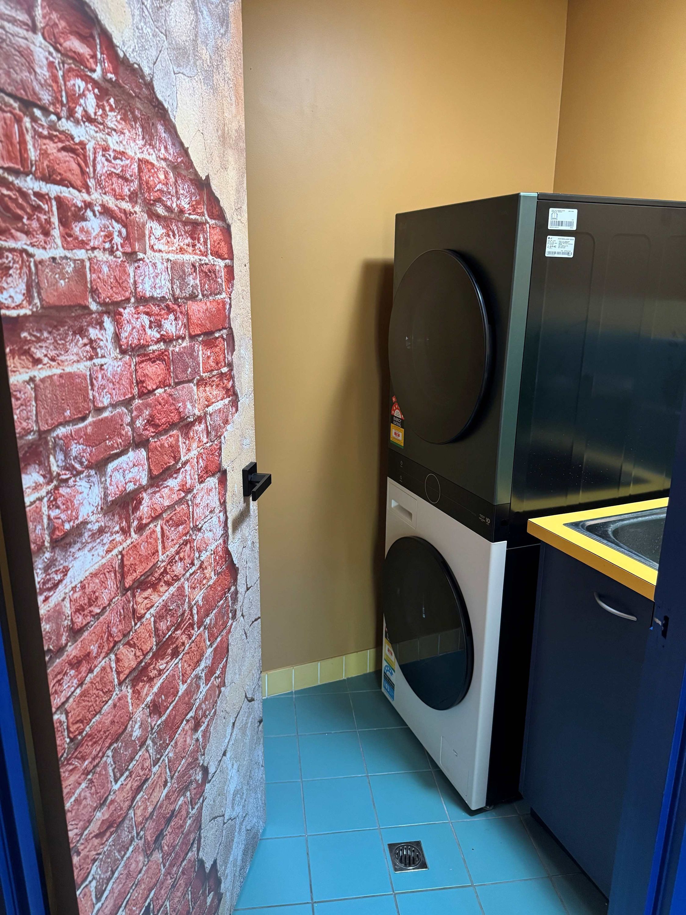 A laundry room with a brick wall, a washing machine, and a dryer stacked on top of each other.