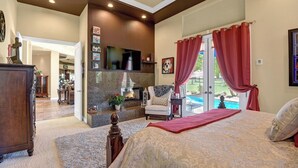Een slaapkamer met een bed, een open haard, een televisie en uitzicht op een zwembad.