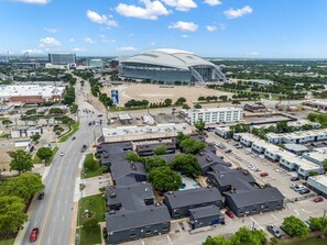 An aerial view of a cityscape with a large stadium, parking lots, and a mix of commercial and residential buildings. - 2BR - AT&T, Globe Life & Texas Live + Parking (Arlington)