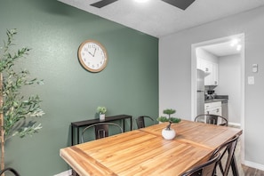 Een eethoek met een houten tafel, stoelen, een klok en een potplant.