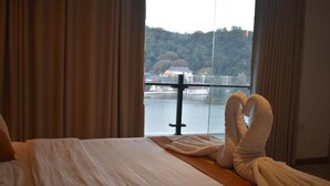 Habitación de hotel con cama, cortinas y vista a un lago y un bosque.