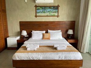 Habitación de hotel con cama de madera, ropa de cama blanca, dos lámparas de noche, una mesita de noche y un cuadro de pájaros en la pared.
