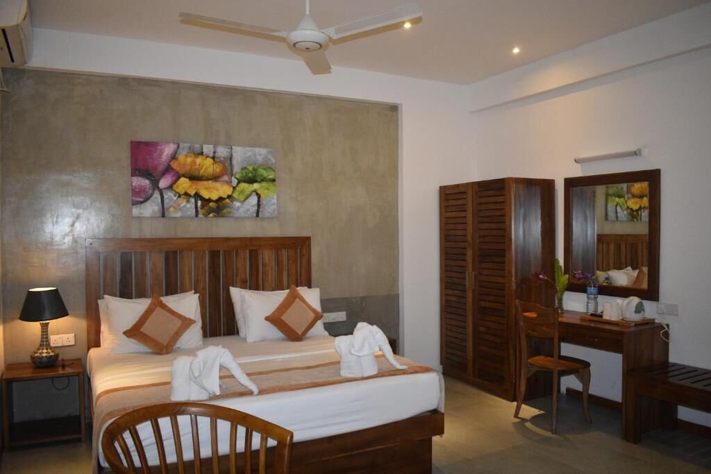 A hotel room with a bed, a desk, a chair, a mirror, and a ceiling fan.