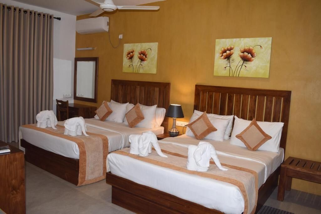 A hotel room with two beds, a bedside table, a lamp, and artwork on the walls.
