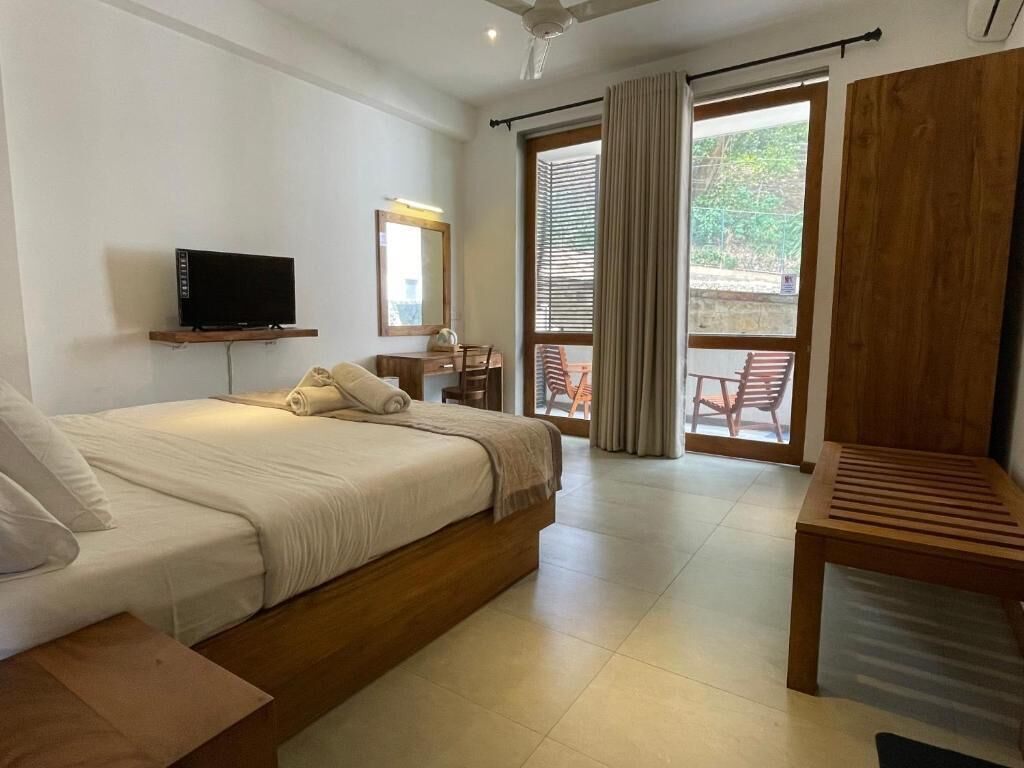 A bedroom with a bed, a TV, a desk, and a view of the outdoors.
