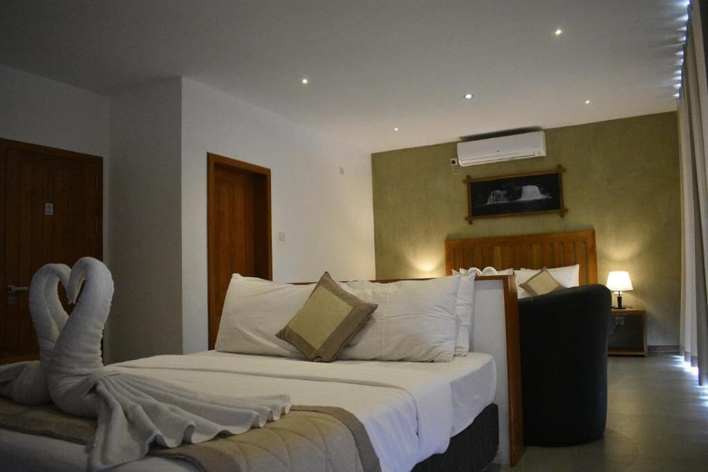 A hotel room with a bed, a chair, a nightstand, and a wall-mounted air conditioning unit.