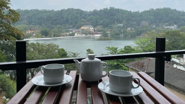 Un balcón con una mesa dispuesta para tomar té, con vista a un lago y una ladera boscosa.