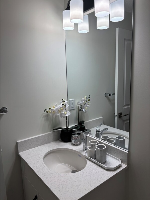 A bathroom with a white sink, a mirror, a potted orchid, and a modern light fixture. - SunnyTimes Escape (Edmonton)