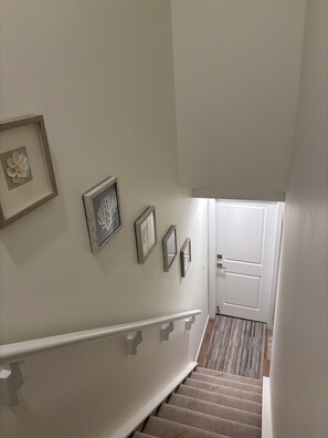 Eine Treppe mit weißer Handlauf, einer Tür am oberen Ende und mehreren gerahmten Bildern an der Wand.
